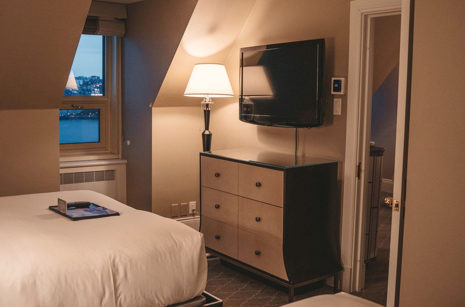 A hotel guest room at dusk with the bedside lamps on